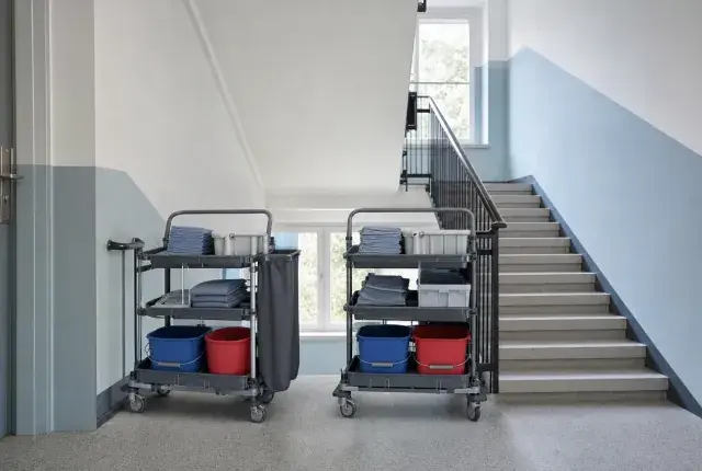 Zwei identisch bestückte Reinigungswagen nebeneinander in einem hellen Treppenhaus mit blauer Wandzone